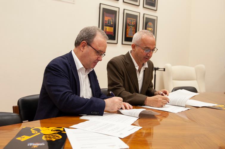 Two men in business attire sitting at a table, signing documents.