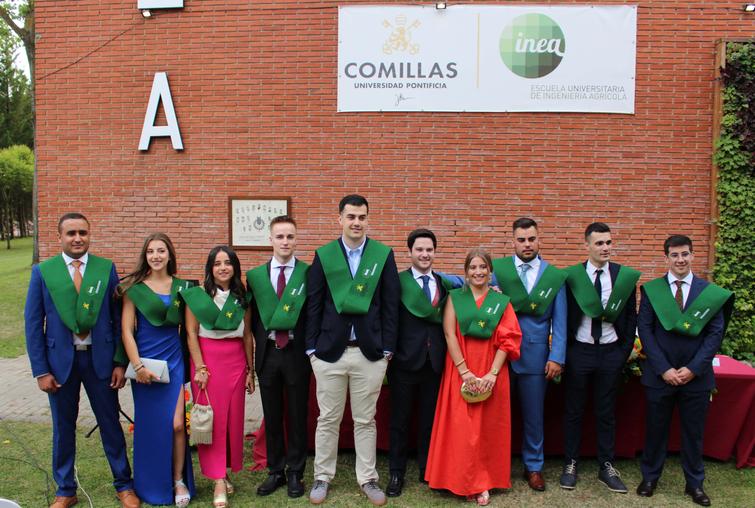 A group of graduates in green sashes posing in front of a university building labeled 'Comillas'