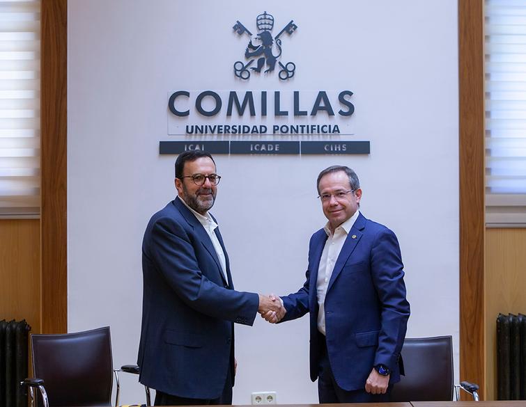 Two men shaking hands in a formal setting with a 'COMILLAS Universidad Pontificia ICAI ICADE' sign in the background.