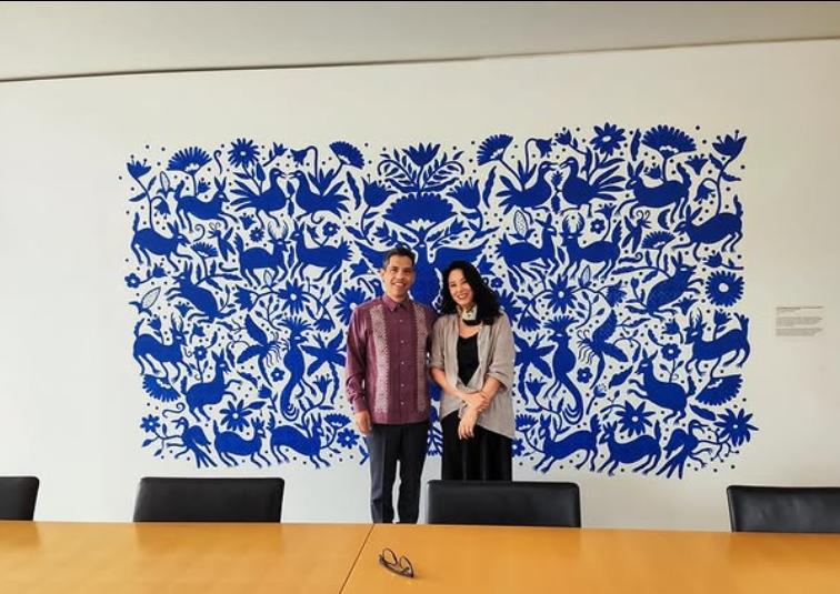 Una pareja posando frente a un mural azul decorado con motivos florales y aves.