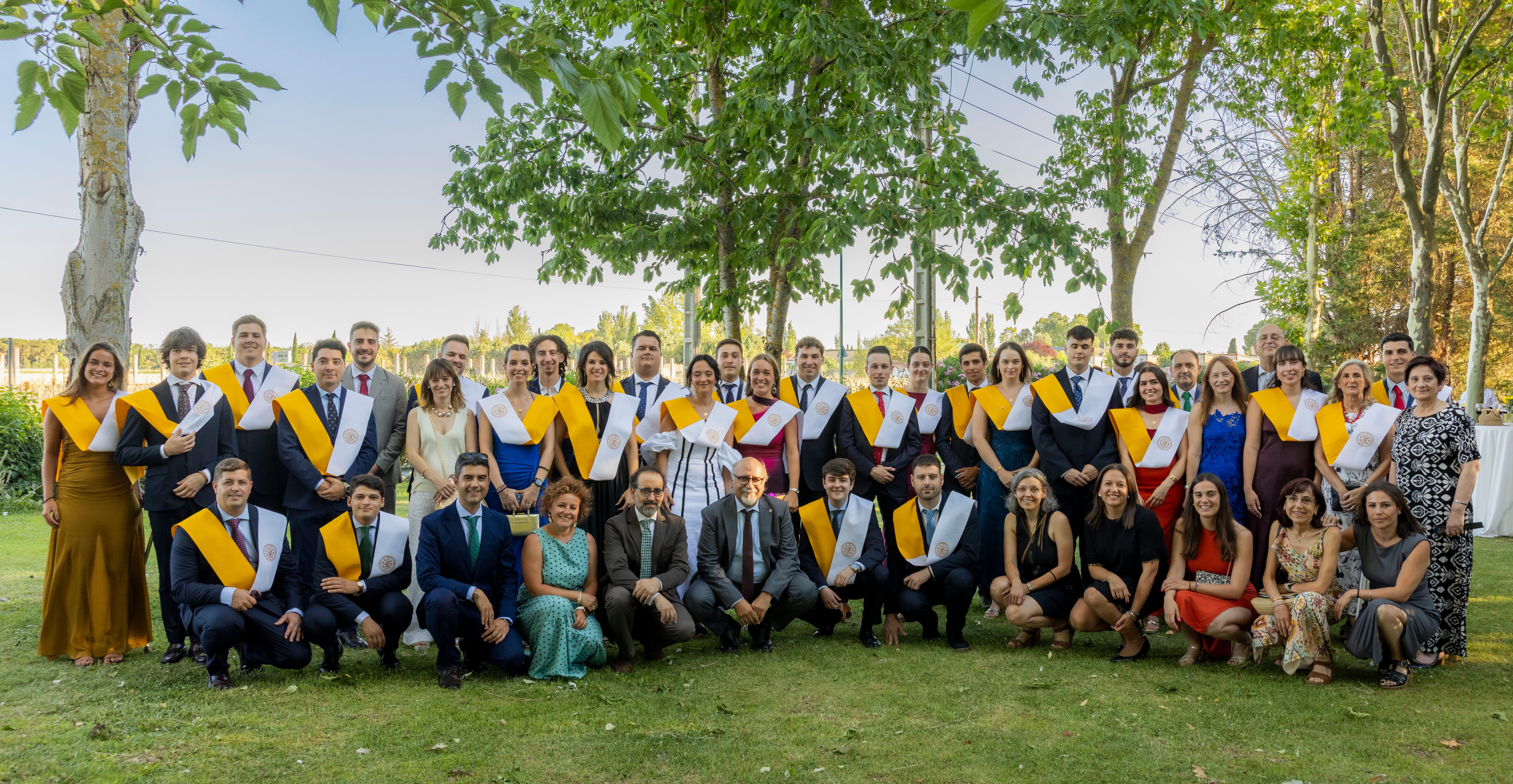 Un grupo de graduados sonríe y posa juntos al aire libre, luciendo togas y birretes, con una atmósfera de celebración.