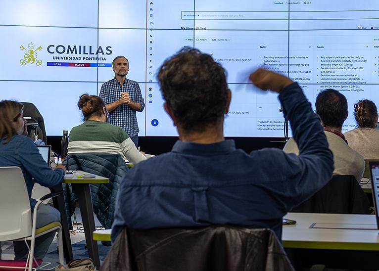 Un hombre dando una conferencia en un aula universitaria con estudiantes y una pantalla grande mostrando información.