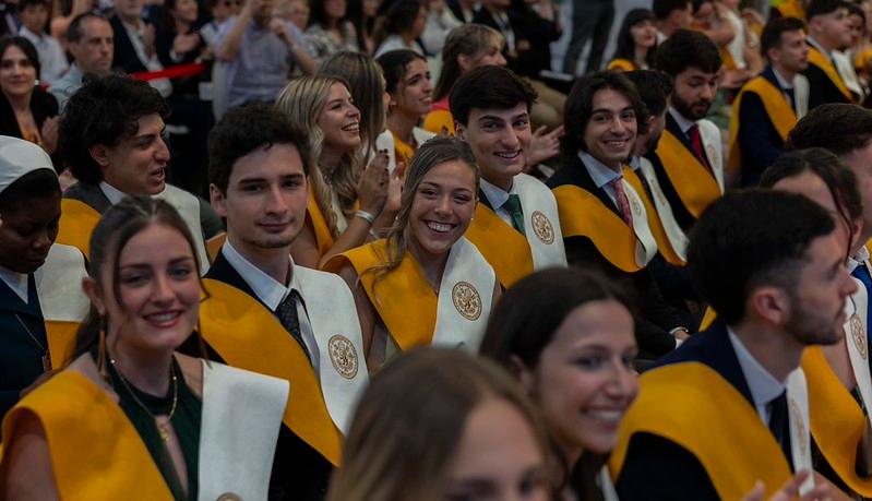 Un grupo de graduados sonríen mientras están sentados en una ceremonia de graduación.