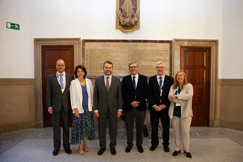 A group of six professionals, three men and three women, standing in a formal pose in an indoor setting with a historical plaque in the background.