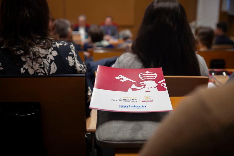 Una persona está sentada en una sala de conferencias con un folleto sobre una mesa en primer plano.