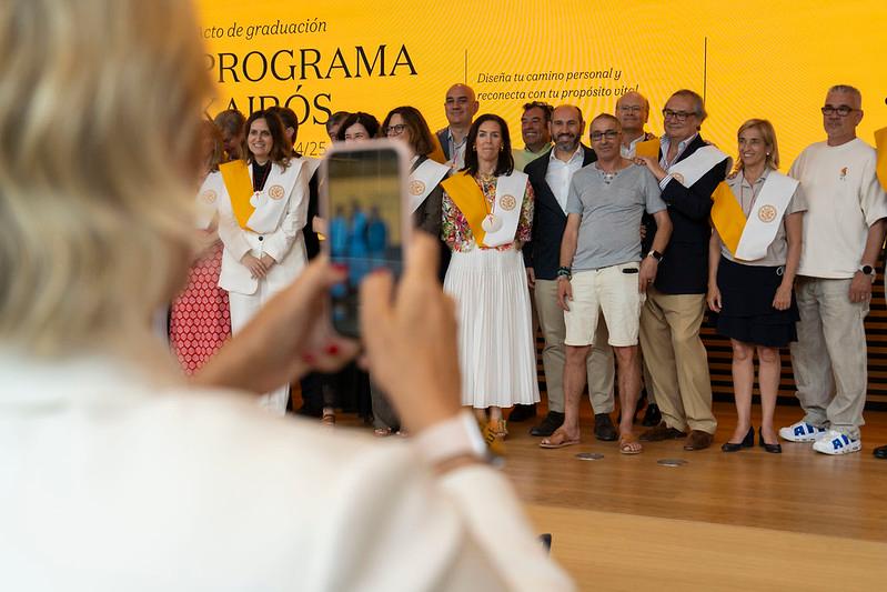Un grupo de personas posando para una foto de graduación con sashes y un fondo decorativo.