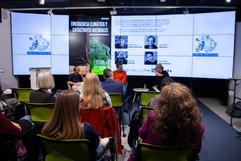 Un panel de discusión sobre emergencia climática y catástrofes naturales, con un público atento en un entorno moderno.