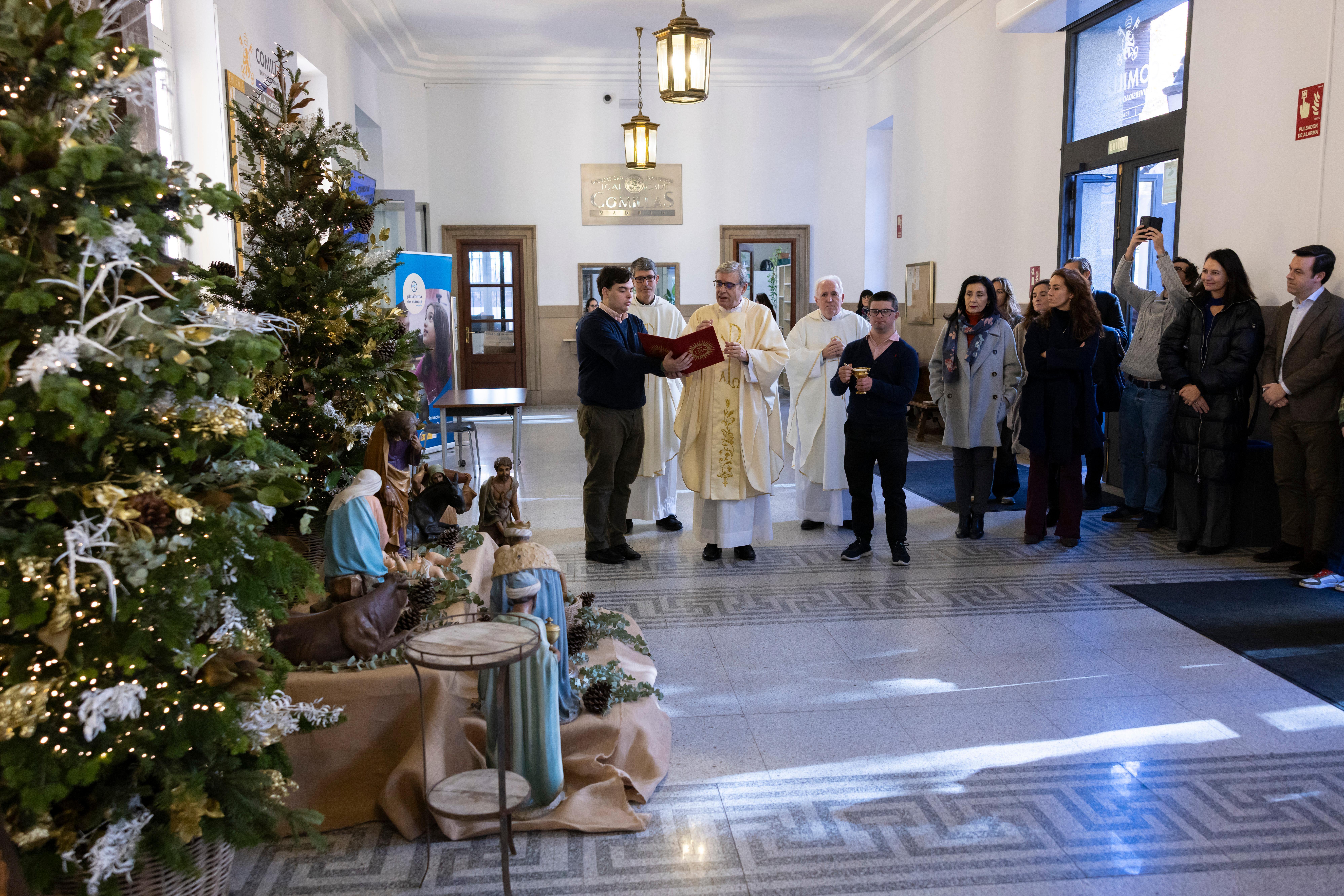 Una ceremonia navideña con un árbol decorado y figuras de Belén en un salón lleno de personas.