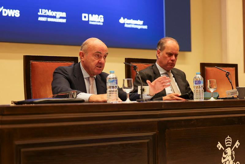 Dos hombres discutiendo en una conferencia con micrófonos y botellas de agua en la mesa.