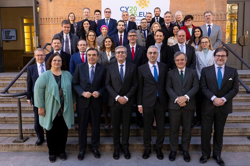 Fotografía de un grupo de personas posando en escaleras frente a un edificio con un cartel de referencia a una conferencia europea.