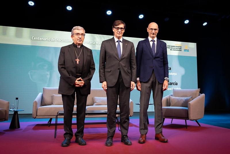Tres hombres posan en un escenario durante un evento con motivo del centenario de un nacimiento.
