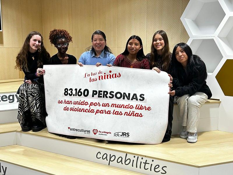 Un grupo de seis mujeres sostiene una pancarta que celebra la unión de 83.160 personas por un mundo libre de violencia para las niñas.