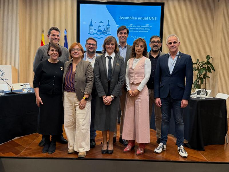 Retrato de los miembros de la Junta Directiva de la UNE 2025-2027 posando ante la pantalla con el programa de la Asamblea General.