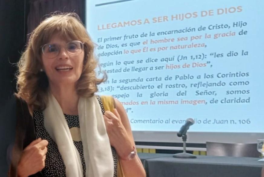 Una mujer sonriente se encuentra junto a una presentación en una conferencia sobre la espiritualidad cristiana.