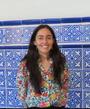 A woman in a floral shirt smiles in front of a blue and white tiled wall.