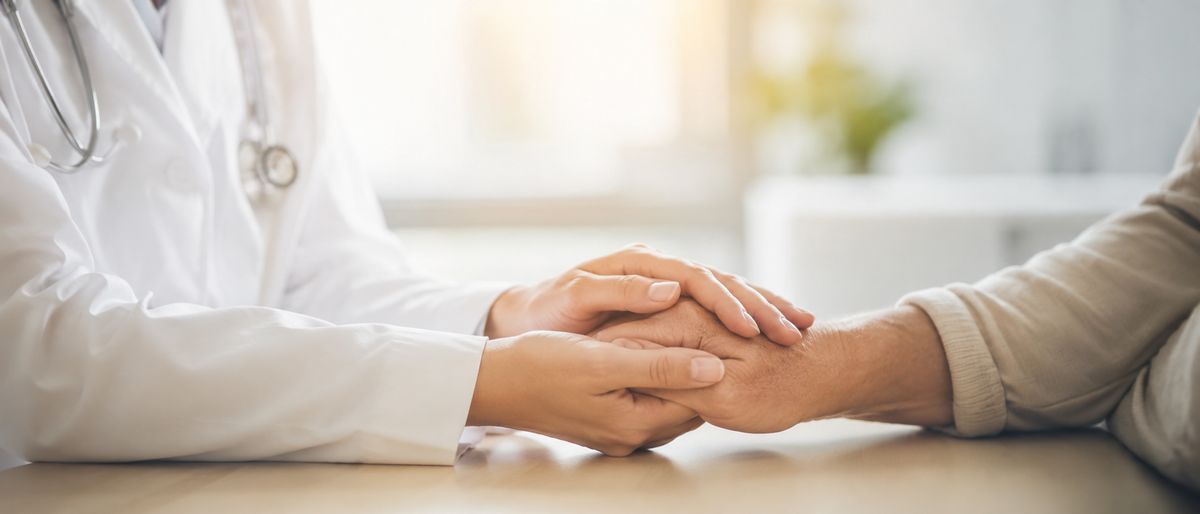 Un médico sostiene la mano de un paciente con gesto de apoyo y empatía.