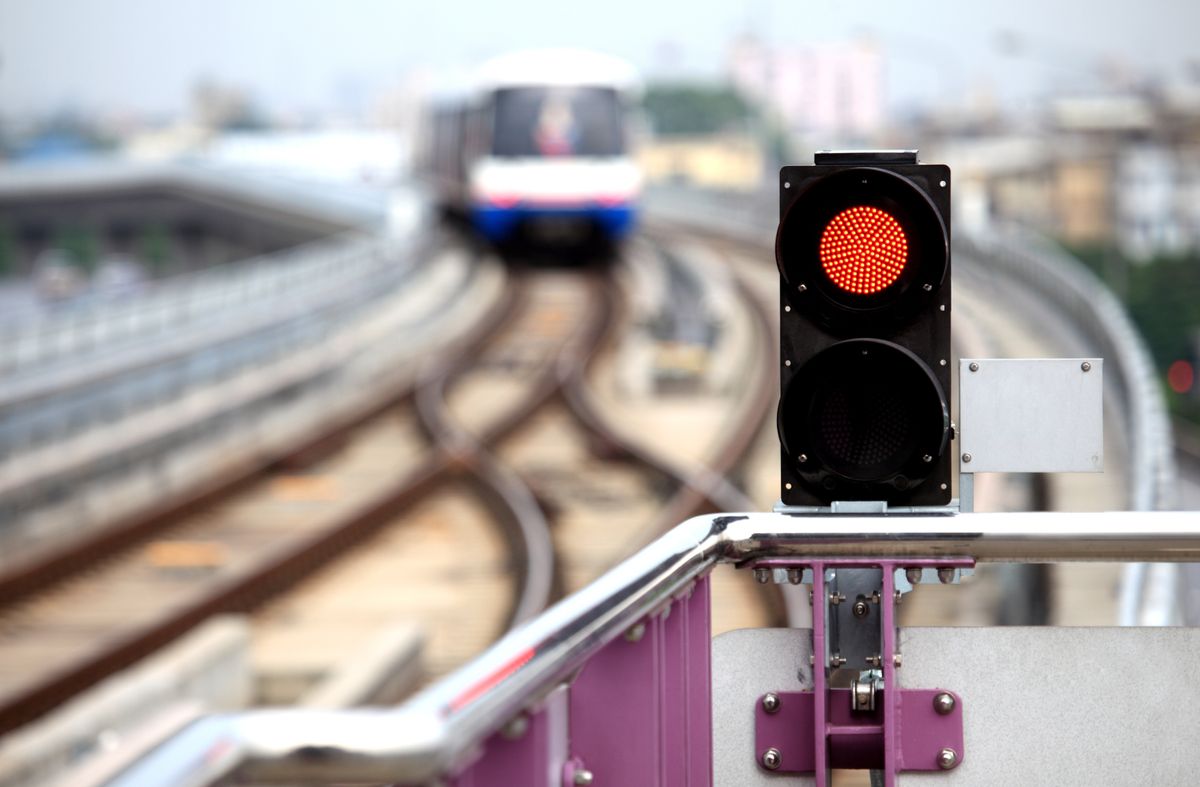 A red traffic signal light in focus with a blurred train approaching on railway tracks in the background.