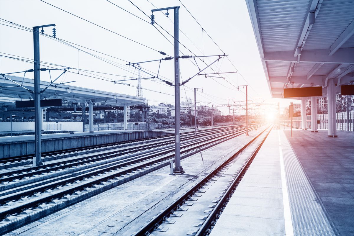 Sunrise view over a railway station with multiple tracks and a platform, in a cool blue tone.