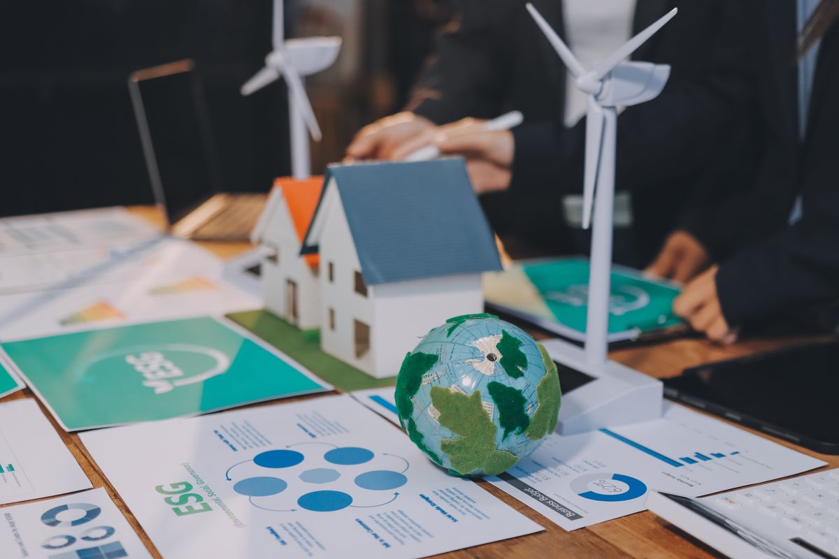Una mesa de trabajo muestra maquetas de casas y turbinas eólicas junto a gráficos relacionados con la sostenibilidad.