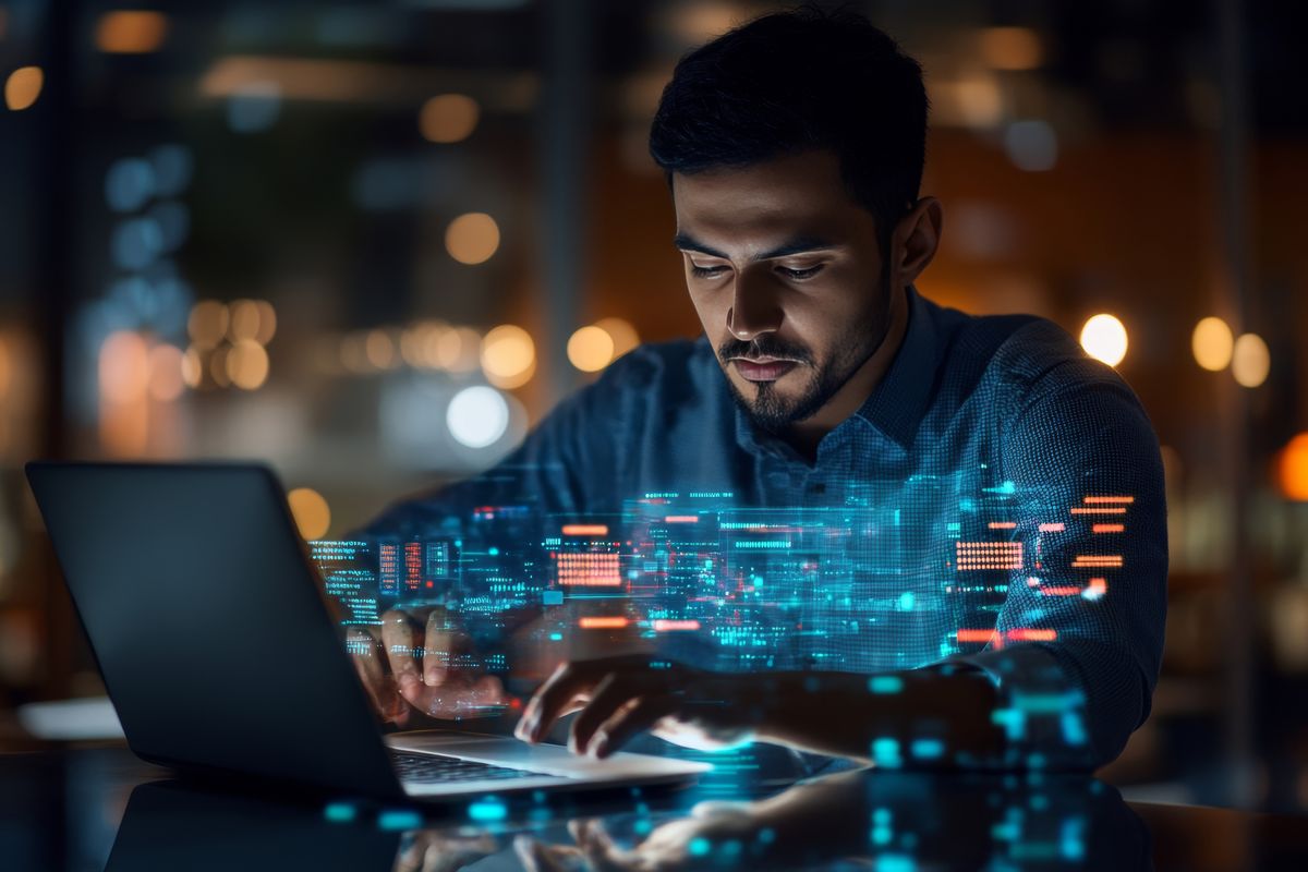 Un hombre trabaja en una laptop mientras interactúa con gráficos digitales que flotan en el aire.