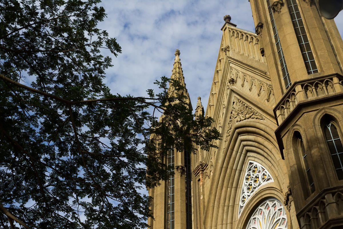La imagen muestra la fachada de una iglesia con detalles arquitectónicos y árboles en primer plano.