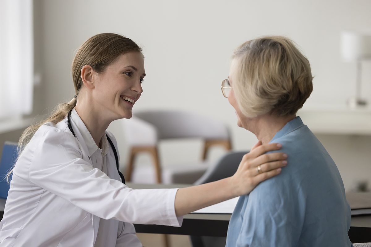 Una médica sonriente conversa con una paciente mayor en una consulta médica.