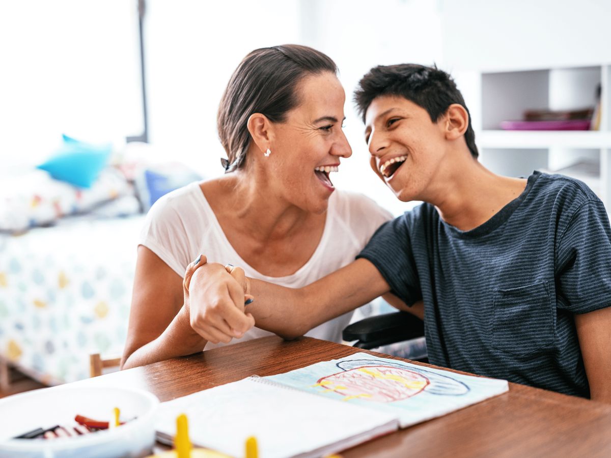 A woman and a young boy smiling at each other while engaged in a fun activity at a table with drawing papers and crayons.