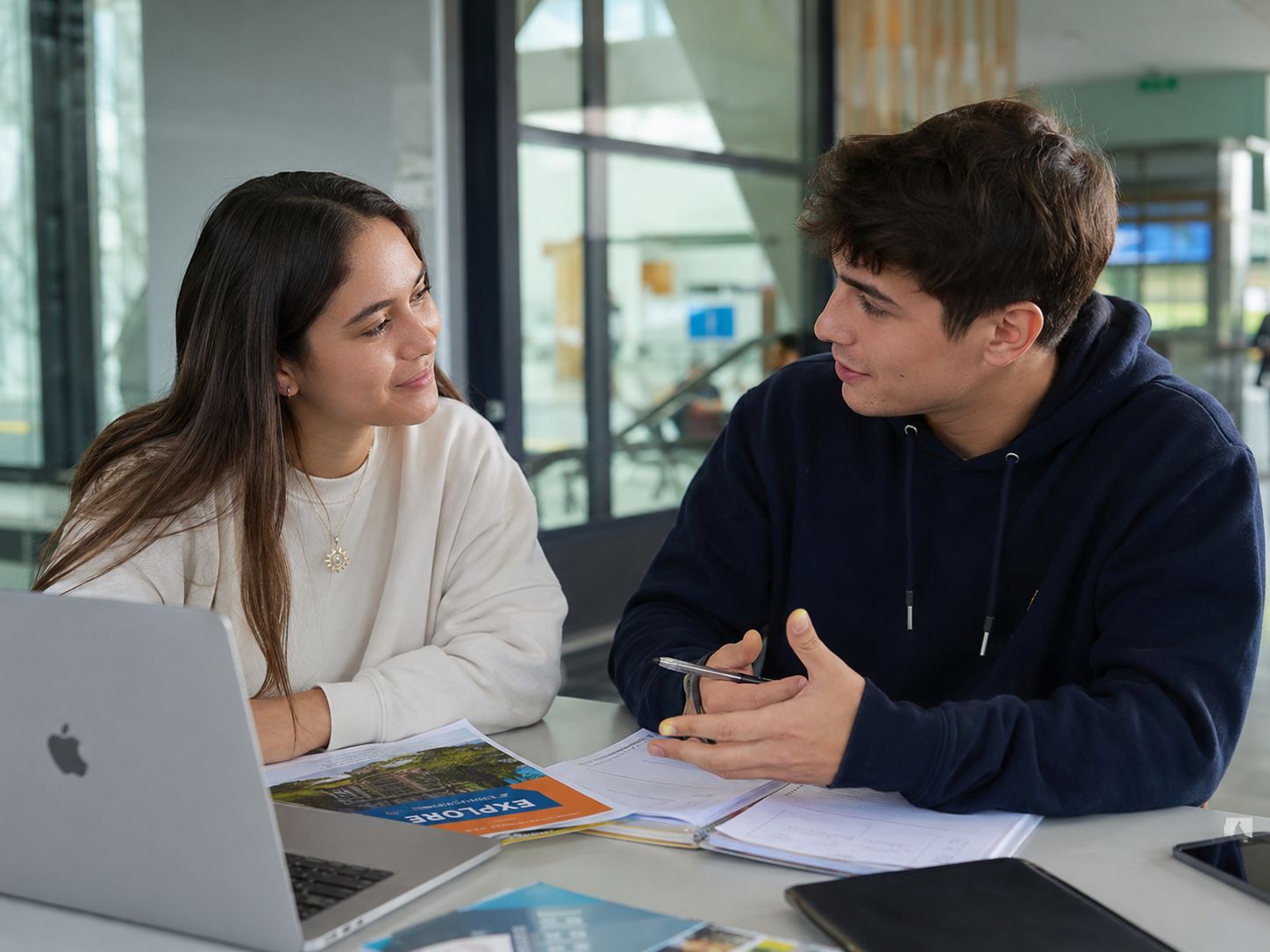 Dos estudiantes conversan y estudian juntos en un ambiente moderno.