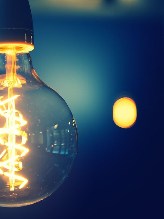 Una bombilla de luz incandescente emitiendo un brillo cálido en un fondo desenfocado.