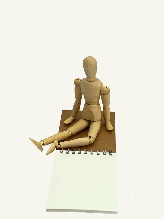 Un maniquí de madera está sentado frente a un cuaderno en blanco.