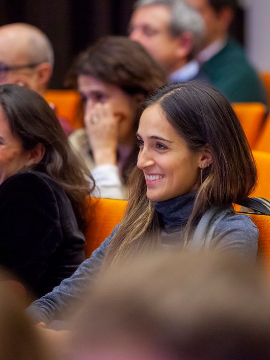 Audience members seated in a conference room, with two smiling women in focus.