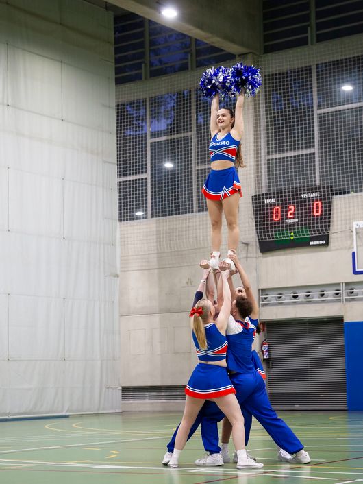 Un grupo de animadoras realizando una pirámide en un gimnasio.