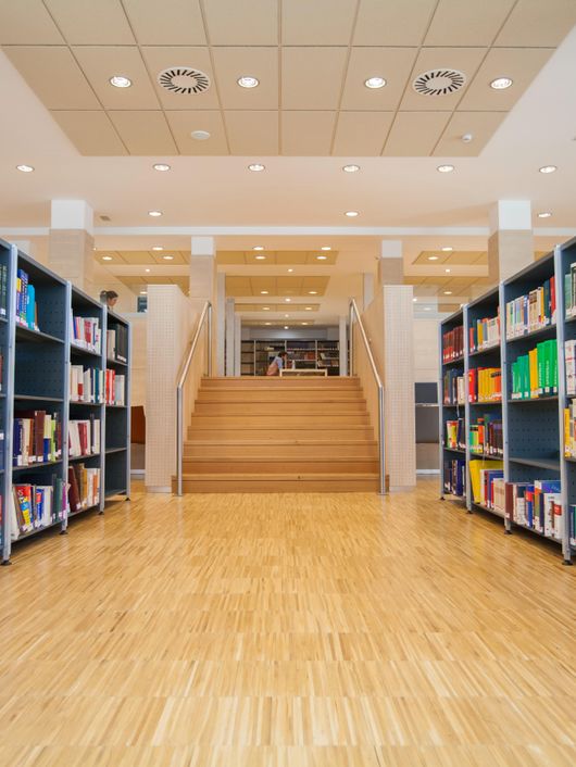 Una biblioteca moderna con estanterías llenas de libros y un área de escaleras al fondo.
