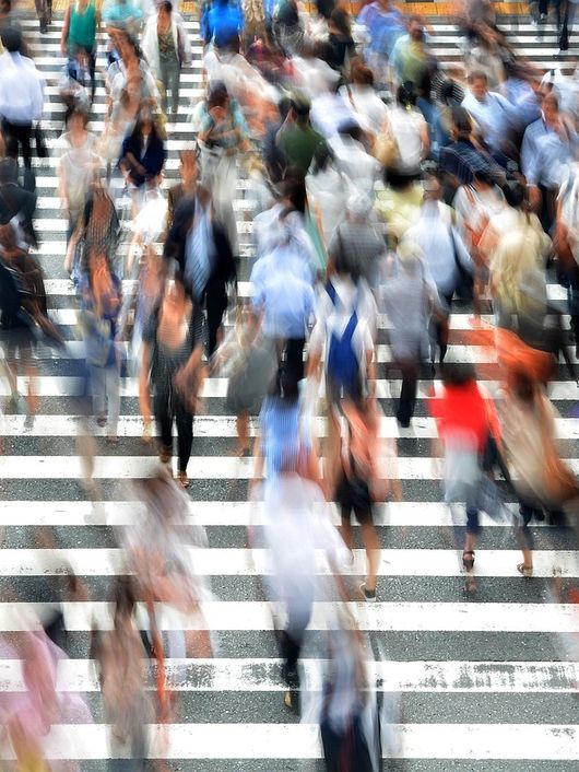Una multitud de personas cruzando una calle con franjas blancas en un entorno urbano.