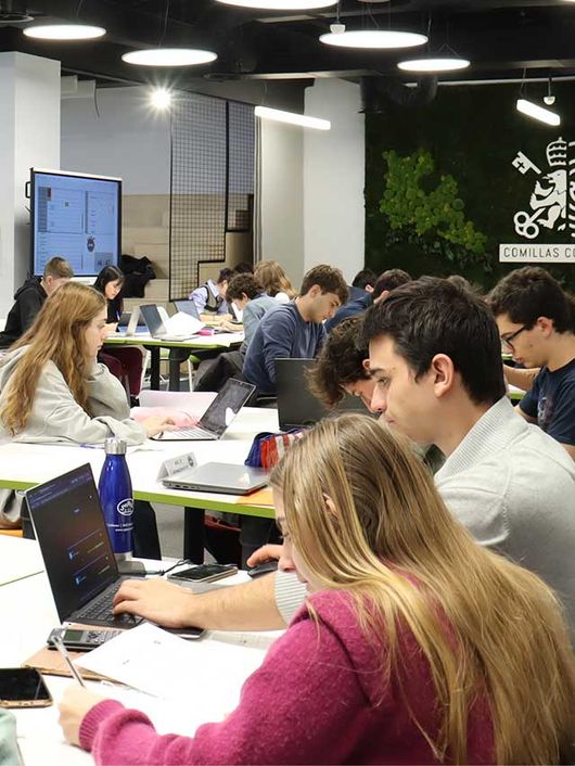 Students studying and working on laptops in a busy university classroom.