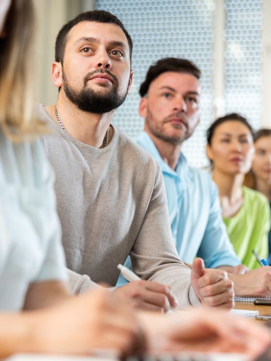 Adult students of diverse backgrounds attentively listening in a classroom setting.