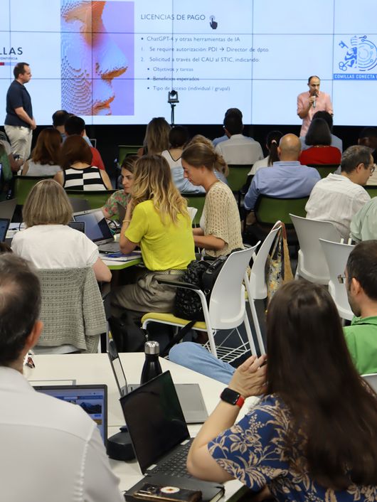 A business presentation in a conference room with attendees using laptops and listening to the presenter.