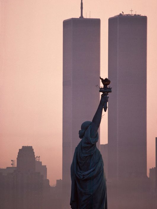 La imagen muestra la Estatua de la Libertad frente a las Torres Gemelas durante el amanecer.