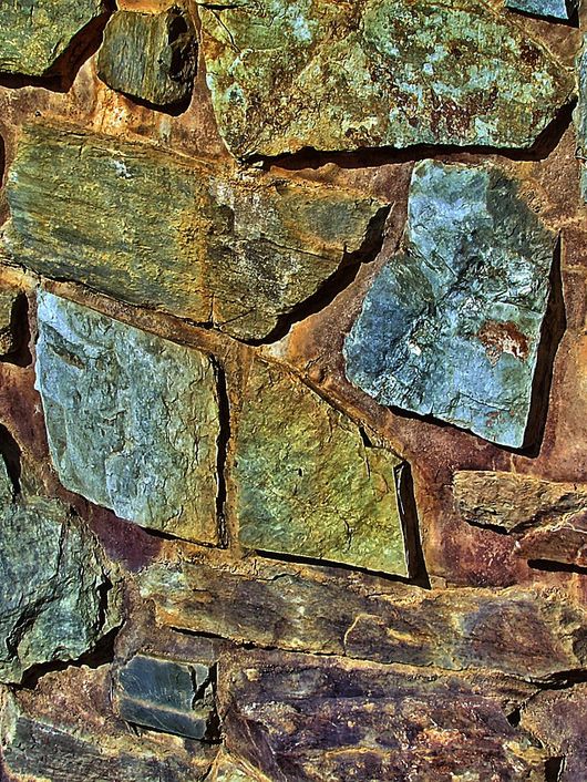 Una pared de piedra compuesta por diversas losas de diferentes colores y texturas.
