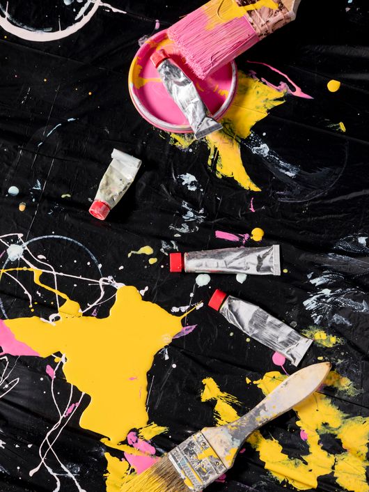 La imagen muestra herramientas de pintura con manchas de colores vibrantes sobre un fondo negro.