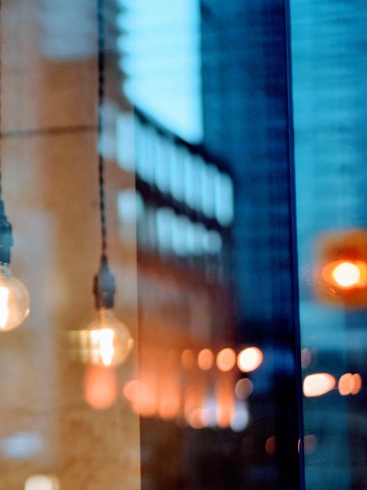 La imagen muestra bombillas colgantes iluminando un ambiente urbano reflejado en una ventana.