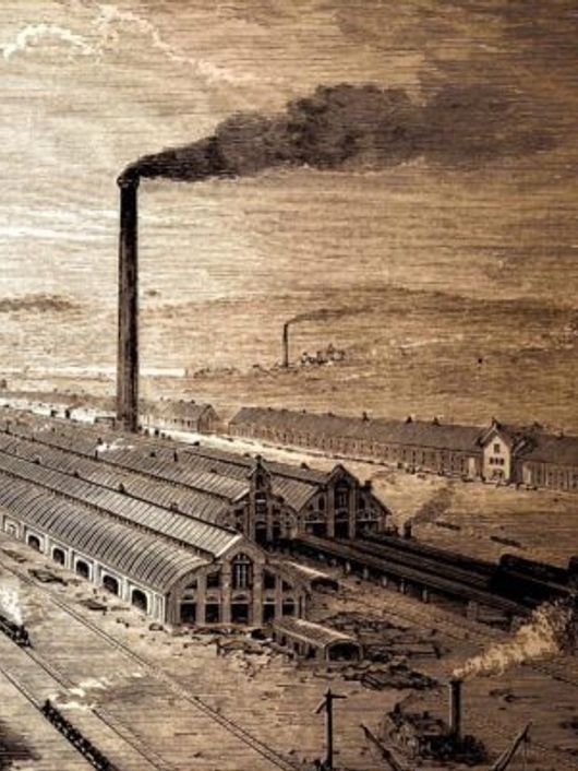 Una vista panorámica de una zona industrial con chimeneas humeantes y vías de tren.