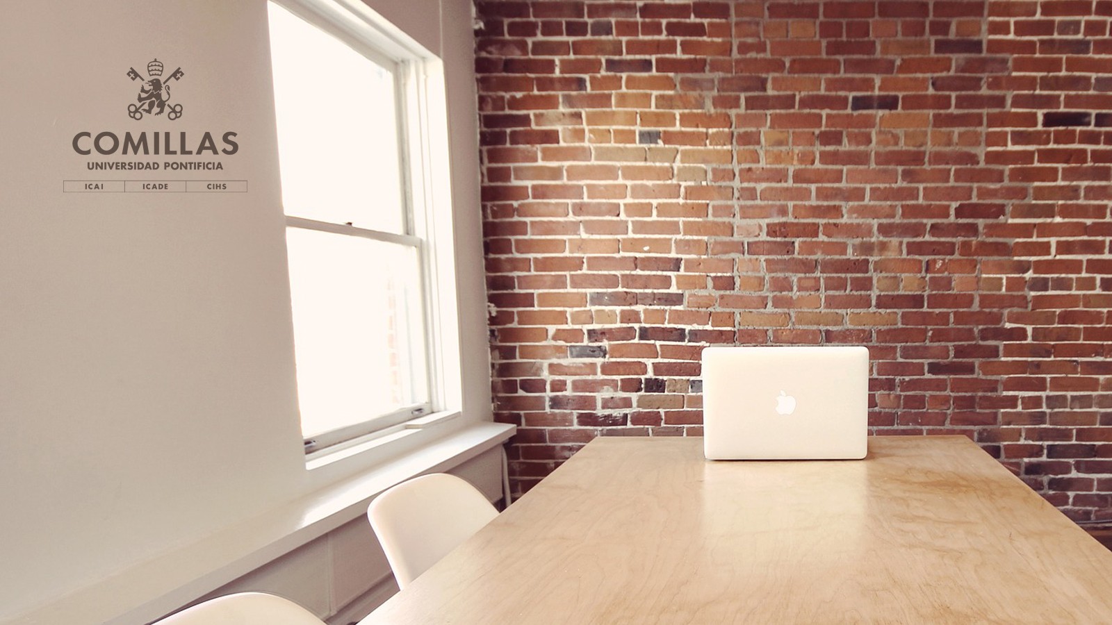 Un espacio de trabajo moderno con una mesa de madera y una laptop sobre ella, rodeado de paredes de ladrillo.