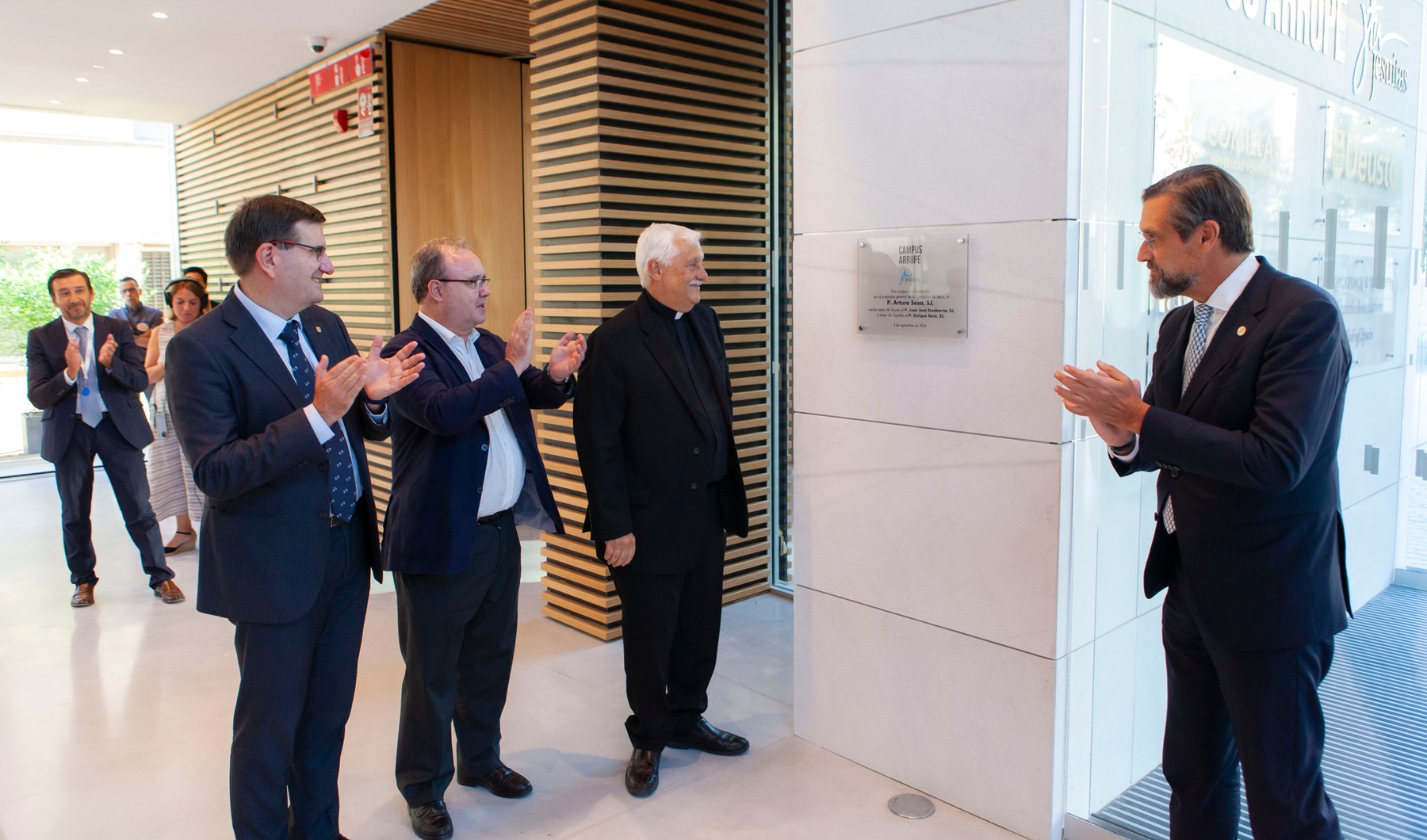 A group of men in suits applauding another man in a corridor.