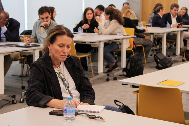 Un grupo de personas está reunido en una sala de conferencias, mientras una mujer toma notas en su cuaderno.