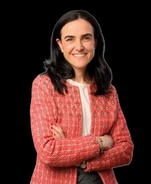 A woman in a red patterned blazer and white blouse stands smiling with her arms crossed against a black background.