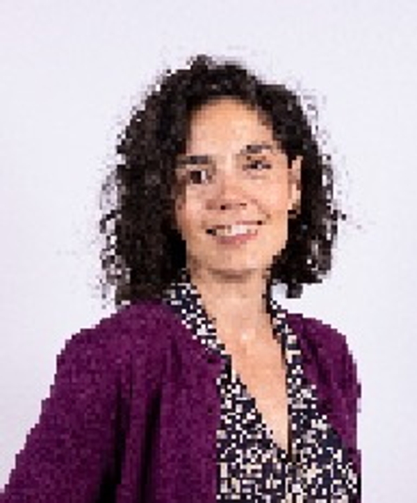 Una mujer sonriente con cabello rizado y un suéter morado que lleva una blusa con estampado.
