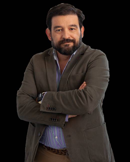 Un hombre con barba y chaqueta se muestra con los brazos cruzados y una expresión serena.