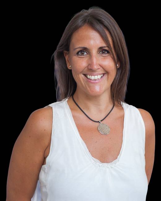 Una mujer sonriente con una blusa blanca y un collar sencillo sobre un fondo negro.