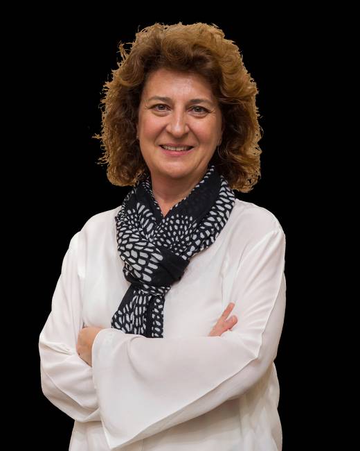 Una mujer sonriente con una camisa blanca y un pañuelo negro presenta una postura confiada.